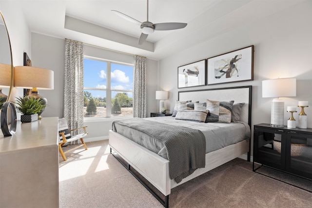 carpeted bedroom with ceiling fan and a tray ceiling