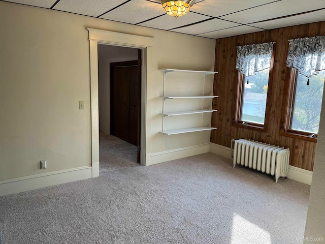 carpeted spare room featuring a paneled ceiling, radiator, and wooden walls