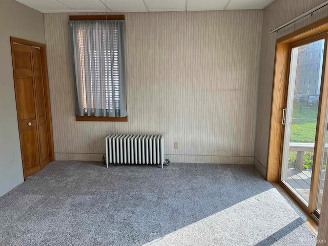 carpeted empty room with a paneled ceiling, a healthy amount of sunlight, and radiator