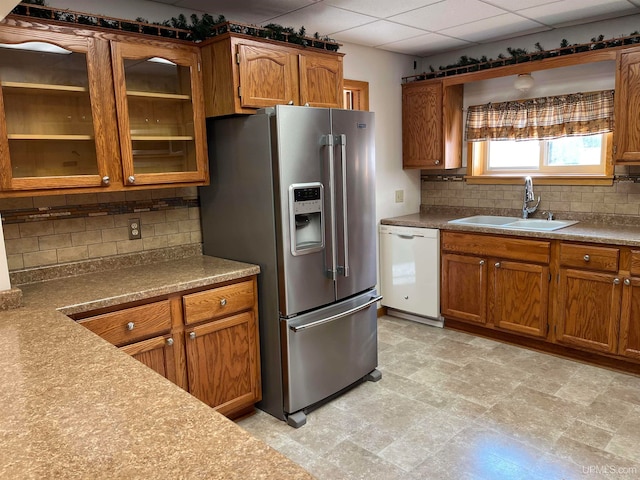 kitchen featuring stainless steel refrigerator with ice dispenser, backsplash, a drop ceiling, white dishwasher, and sink