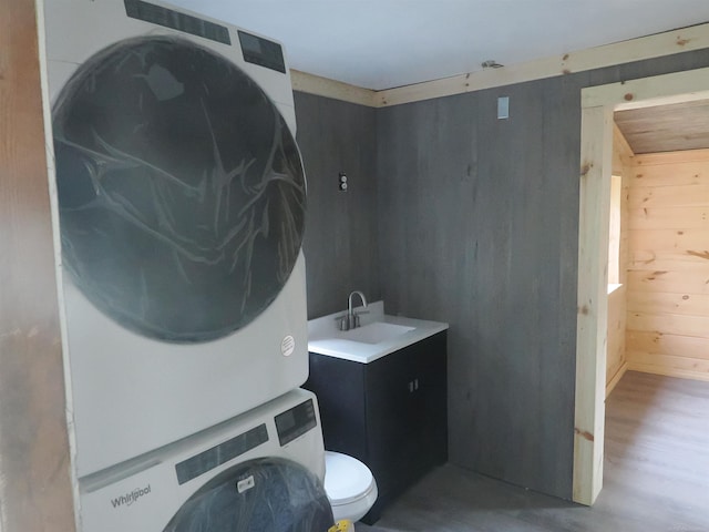 washroom featuring sink, wooden walls, hardwood / wood-style floors, and stacked washer / drying machine