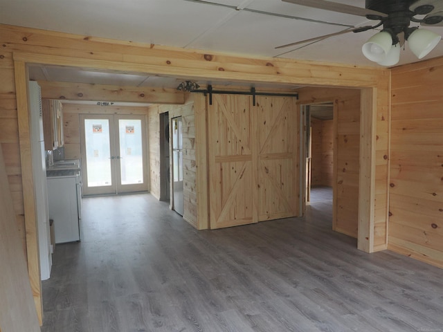 spare room featuring a barn door, ceiling fan, wooden walls, french doors, and hardwood / wood-style flooring