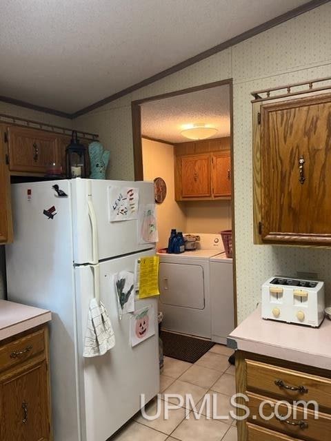 kitchen with light tile patterned floors, ornamental molding, washing machine and clothes dryer, a textured ceiling, and white fridge