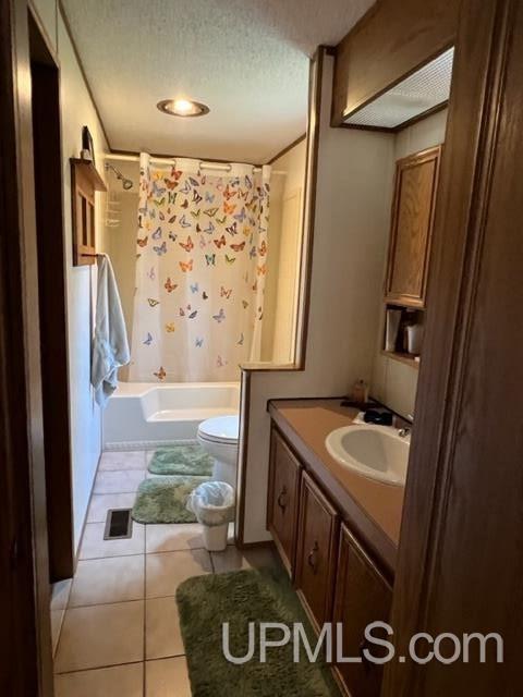 full bathroom with vanity, shower / bath combo, a textured ceiling, tile patterned floors, and toilet