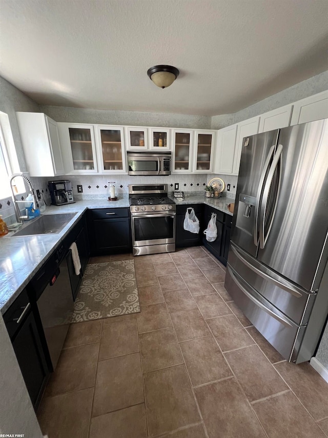 kitchen with appliances with stainless steel finishes, white cabinets, tasteful backsplash, and sink