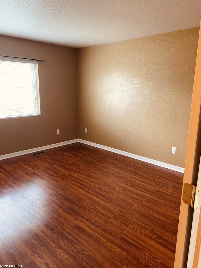 empty room with dark hardwood / wood-style floors and a textured ceiling