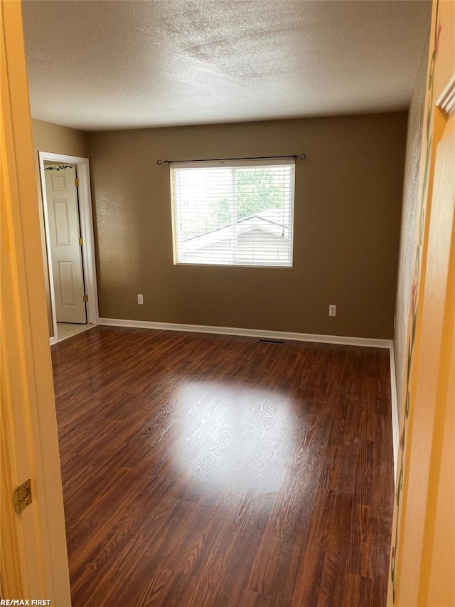 spare room featuring dark wood-type flooring and a textured ceiling