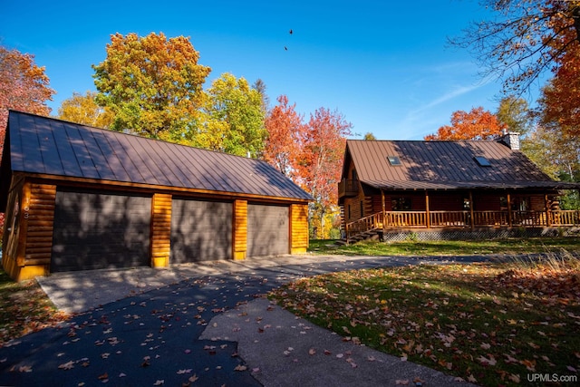 log-style house featuring a garage, covered porch, and an outbuilding