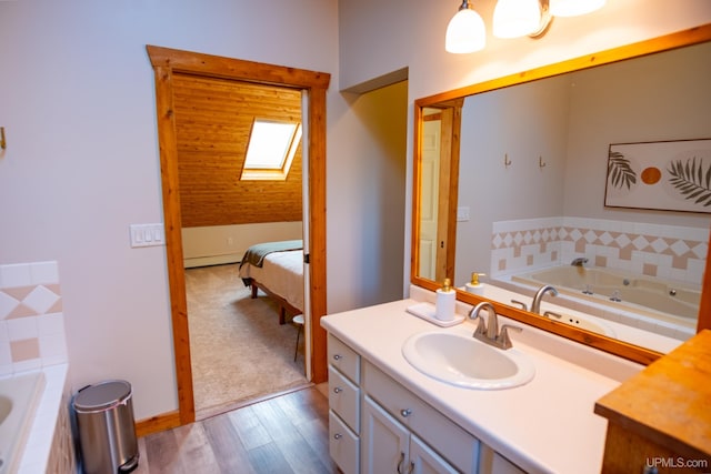 bathroom featuring a skylight, vanity, a relaxing tiled tub, baseboard heating, and hardwood / wood-style flooring