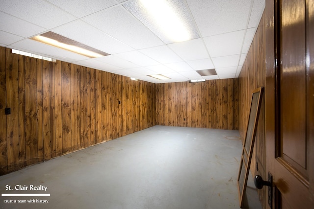 basement featuring a drop ceiling and wooden walls