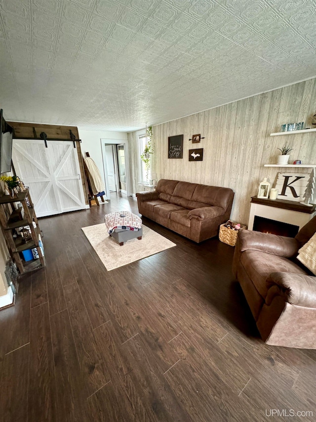 unfurnished living room with a textured ceiling, wooden walls, a barn door, and dark hardwood / wood-style flooring