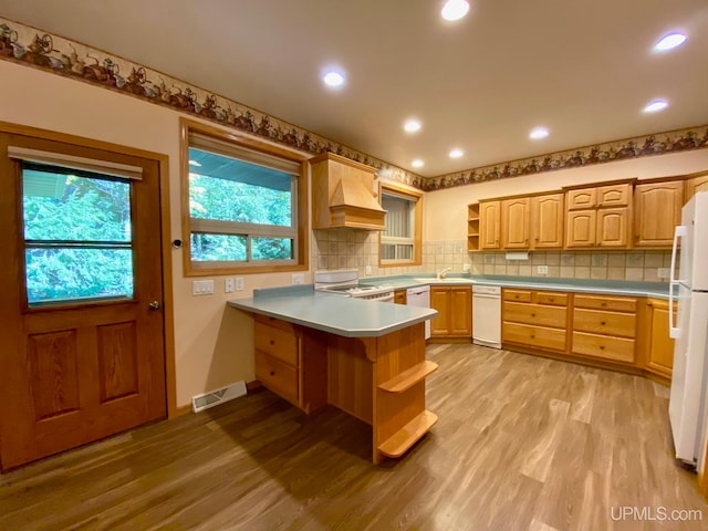 kitchen with white appliances, light wood-type flooring, backsplash, kitchen peninsula, and custom range hood