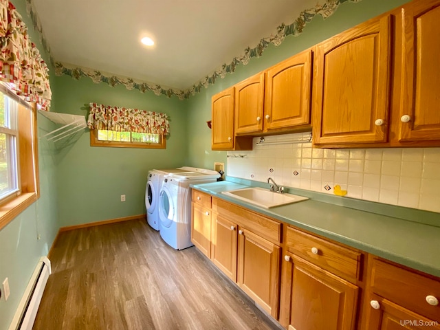 clothes washing area with a baseboard heating unit, sink, light wood-type flooring, cabinets, and washer and dryer