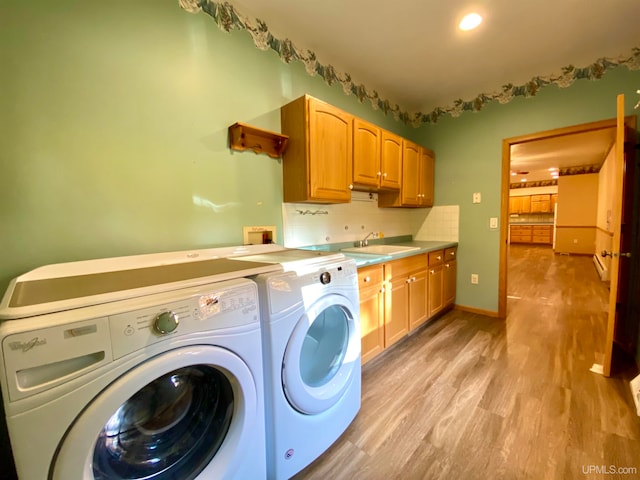 clothes washing area featuring sink, washer and clothes dryer, light hardwood / wood-style flooring, and cabinets