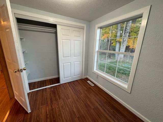 unfurnished bedroom featuring a textured ceiling, dark hardwood / wood-style floors, and a closet