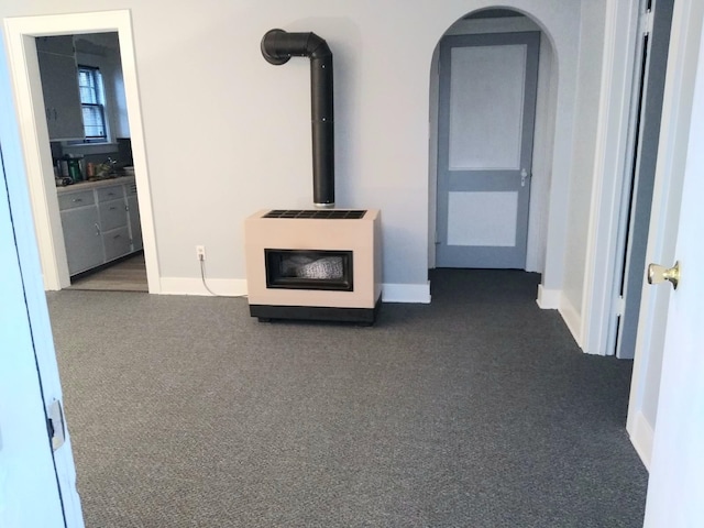 unfurnished living room featuring a wood stove, heating unit, and dark carpet