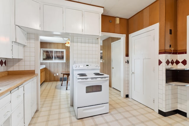 kitchen with wood walls, tasteful backsplash, electric range, and white cabinets