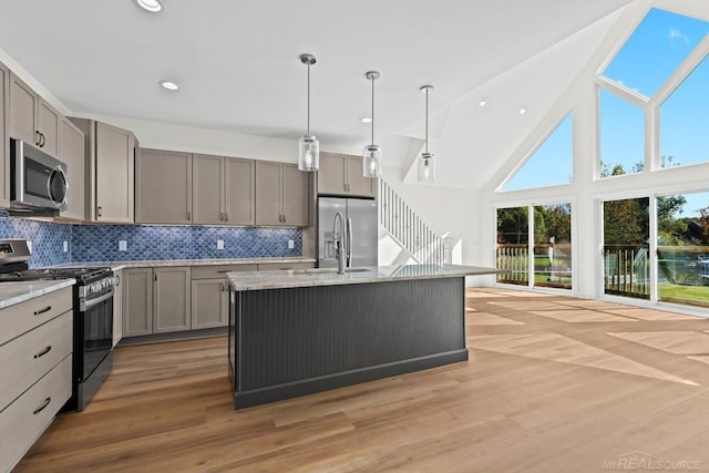 kitchen featuring light stone countertops, light wood-type flooring, appliances with stainless steel finishes, and an island with sink