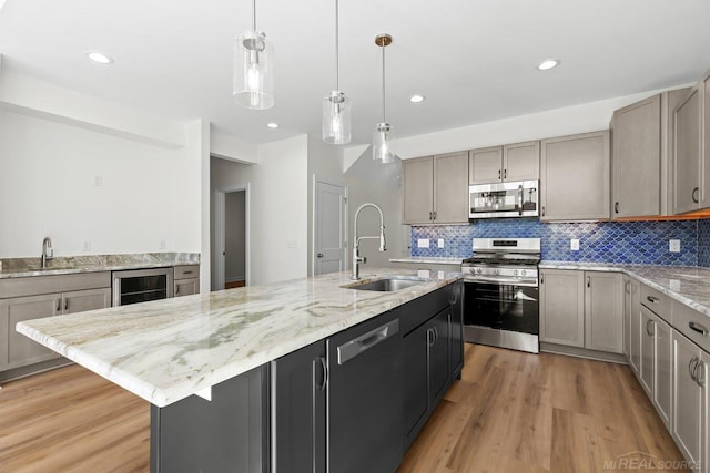 kitchen featuring hardwood / wood-style floors, beverage cooler, a center island with sink, sink, and stainless steel appliances