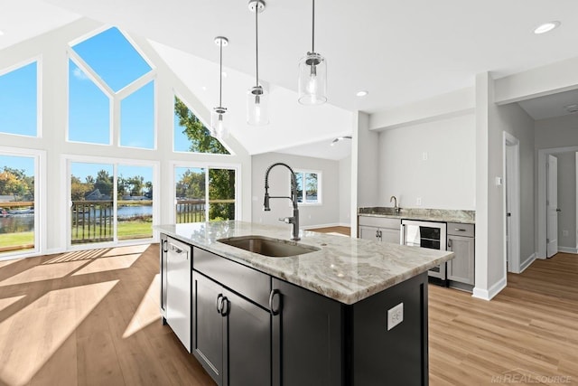 kitchen with sink, light stone counters, light hardwood / wood-style floors, pendant lighting, and wine cooler