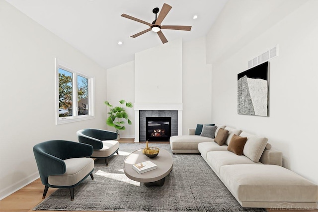 living room with ceiling fan, a tiled fireplace, high vaulted ceiling, and hardwood / wood-style floors