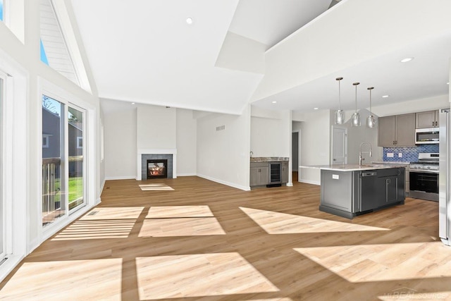 kitchen with hanging light fixtures, an island with sink, appliances with stainless steel finishes, light hardwood / wood-style flooring, and gray cabinets