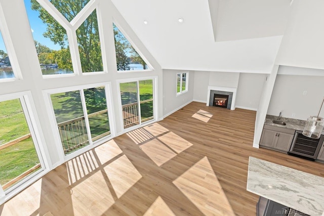 unfurnished living room featuring a healthy amount of sunlight, a towering ceiling, light wood-type flooring, and beverage cooler