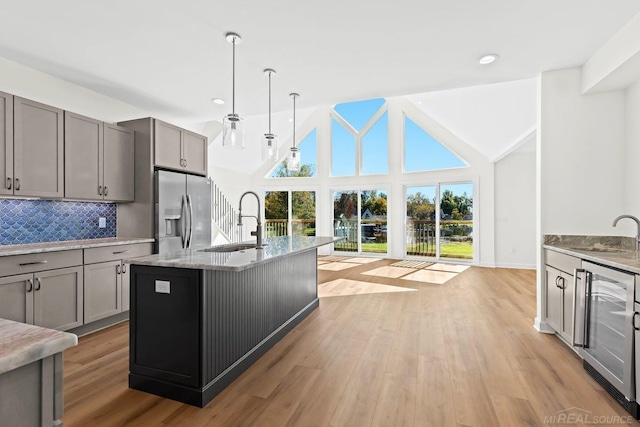 kitchen featuring stainless steel fridge, hanging light fixtures, beverage cooler, a center island with sink, and light wood-type flooring