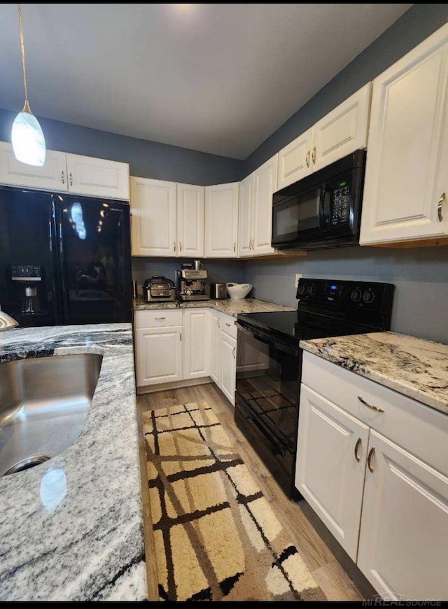 kitchen with hanging light fixtures, black appliances, light wood-type flooring, and white cabinets