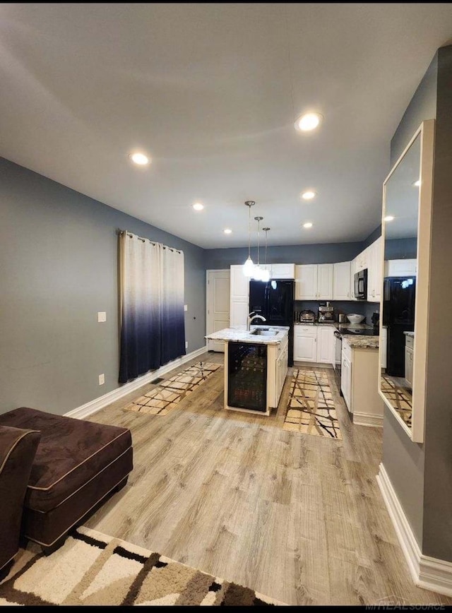 kitchen with black fridge, an island with sink, decorative light fixtures, light wood-type flooring, and white cabinetry