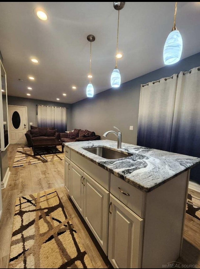 kitchen featuring an island with sink, sink, pendant lighting, light hardwood / wood-style floors, and light stone counters