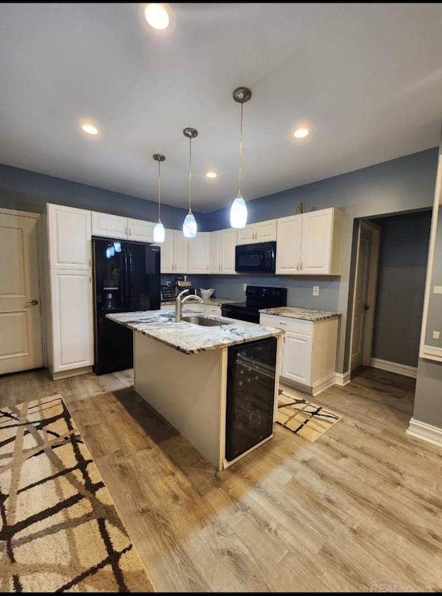 kitchen featuring white cabinetry, a kitchen island with sink, black appliances, light hardwood / wood-style floors, and sink