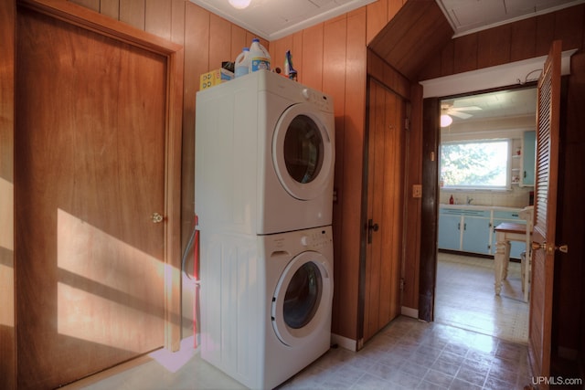 laundry area featuring stacked washer / drying machine, wood walls, sink, and ceiling fan