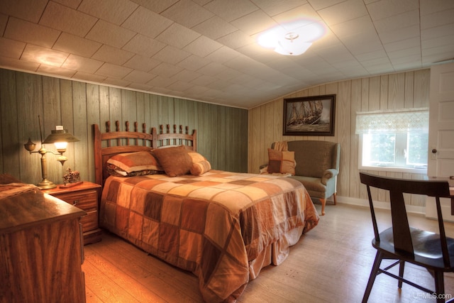 bedroom with lofted ceiling, light wood-type flooring, and wood walls