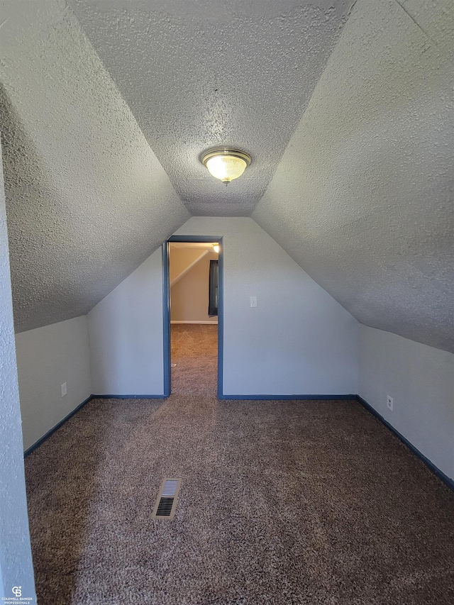 additional living space featuring a textured ceiling, dark carpet, and vaulted ceiling