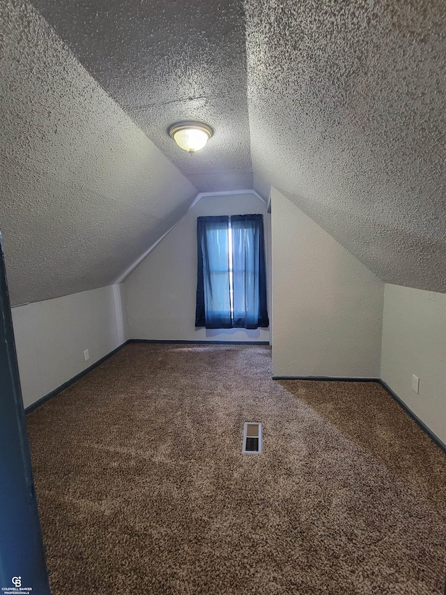 additional living space featuring vaulted ceiling, a textured ceiling, and carpet floors