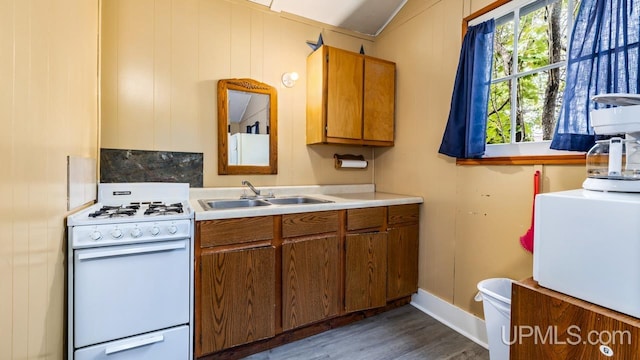 kitchen with white gas range oven, sink, dark hardwood / wood-style floors, and wood walls