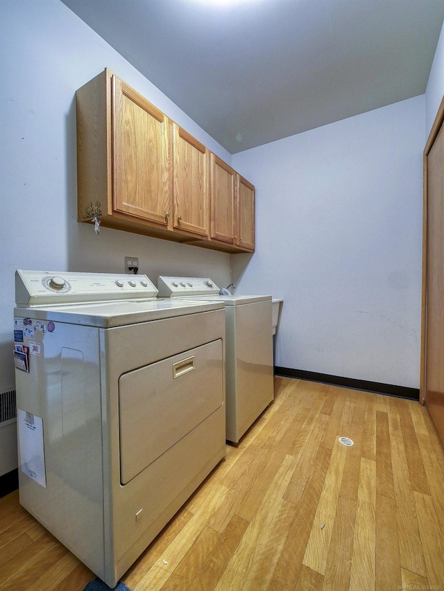 laundry room featuring light hardwood / wood-style flooring, washing machine and clothes dryer, and cabinets