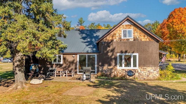 back of property with a yard, stone siding, a patio, and metal roof