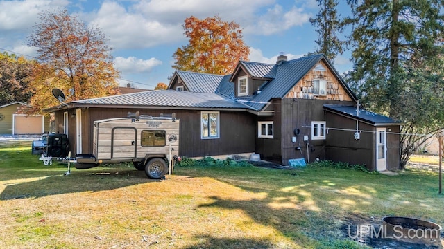 rear view of house featuring a lawn, a fire pit, a chimney, and metal roof