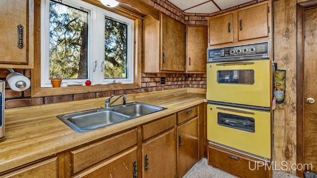 kitchen with double wall oven, brown cabinetry, wood counters, and a sink