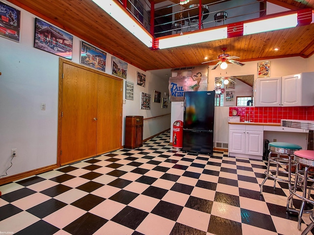 kitchen featuring backsplash, black fridge, wood ceiling, ceiling fan, and white cabinetry