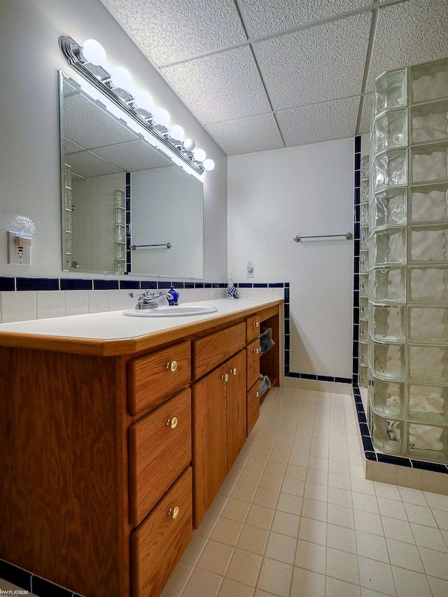 bathroom featuring a drop ceiling, vanity, tile patterned floors, decorative backsplash, and walk in shower