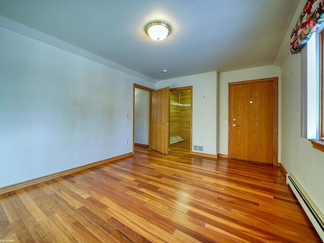 unfurnished bedroom featuring baseboard heating and light hardwood / wood-style flooring