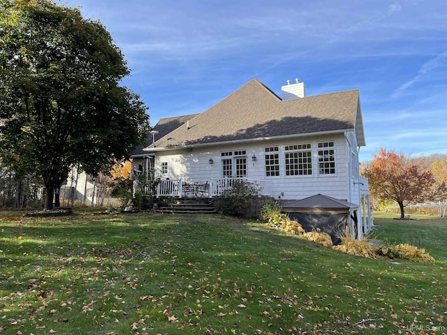 rear view of house with a lawn, a chimney, roof with shingles, and a deck