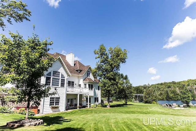 rear view of house featuring a yard, a chimney, and a water view