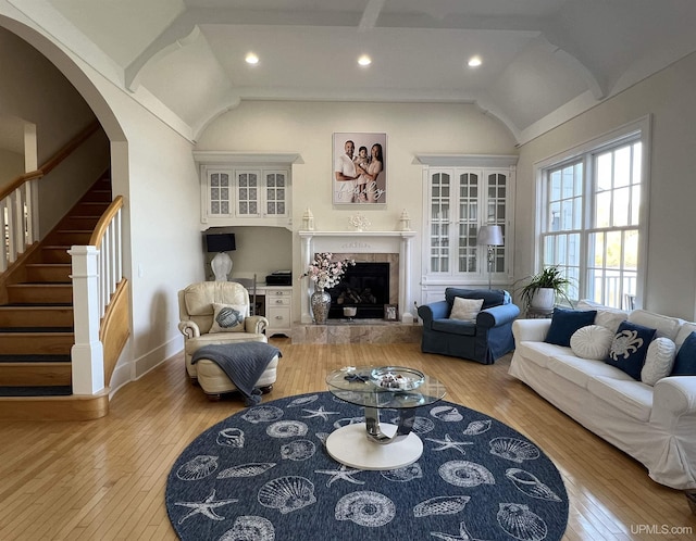 living room with lofted ceiling, hardwood / wood-style flooring, arched walkways, and stairway