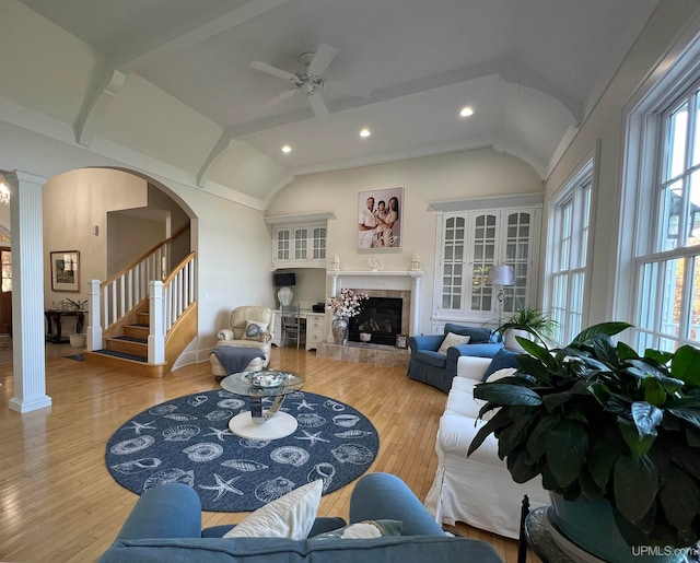 living room with lofted ceiling with beams, decorative columns, a tiled fireplace, ceiling fan, and light hardwood / wood-style flooring