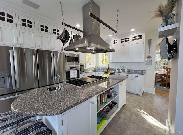 kitchen with appliances with stainless steel finishes, sink, an island with sink, island range hood, and dark stone counters