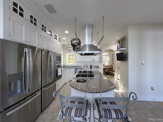kitchen with an island with sink, island exhaust hood, arched walkways, stainless steel appliances, and white cabinets